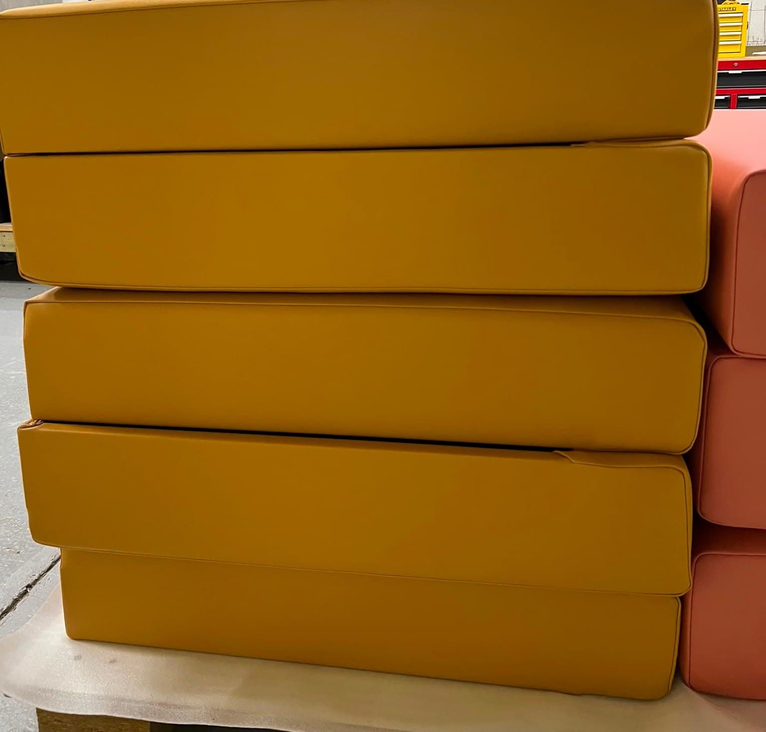 A run of bench cushions in ochre, stacked in the workroom